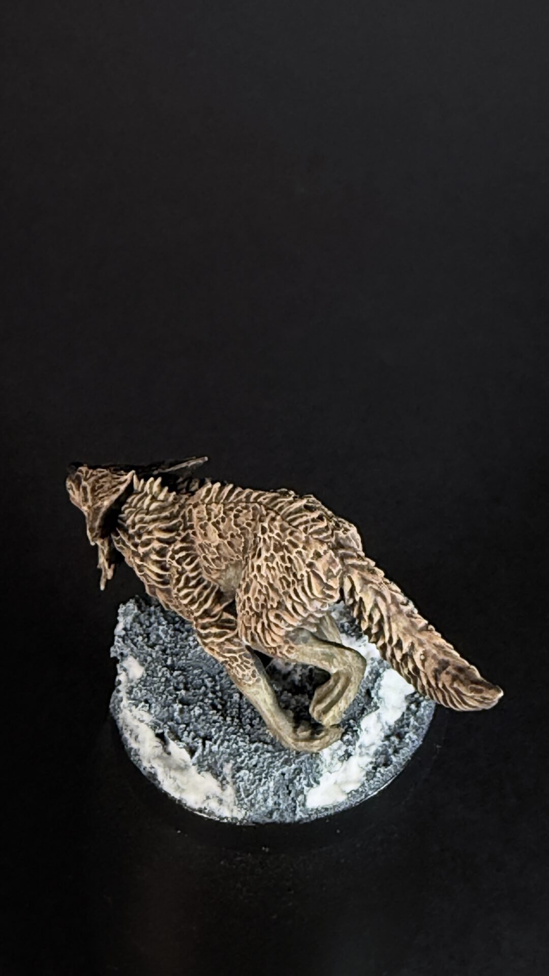 Brown textured lizard sculpture perched on a rocky base against a black background.