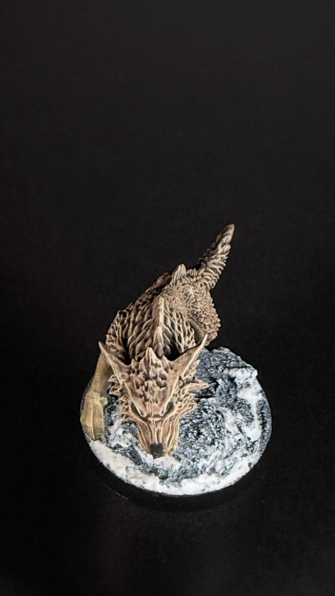 Close-up of a detailed dragon head sculpture perched atop a round, rocky pedestal against a black background.