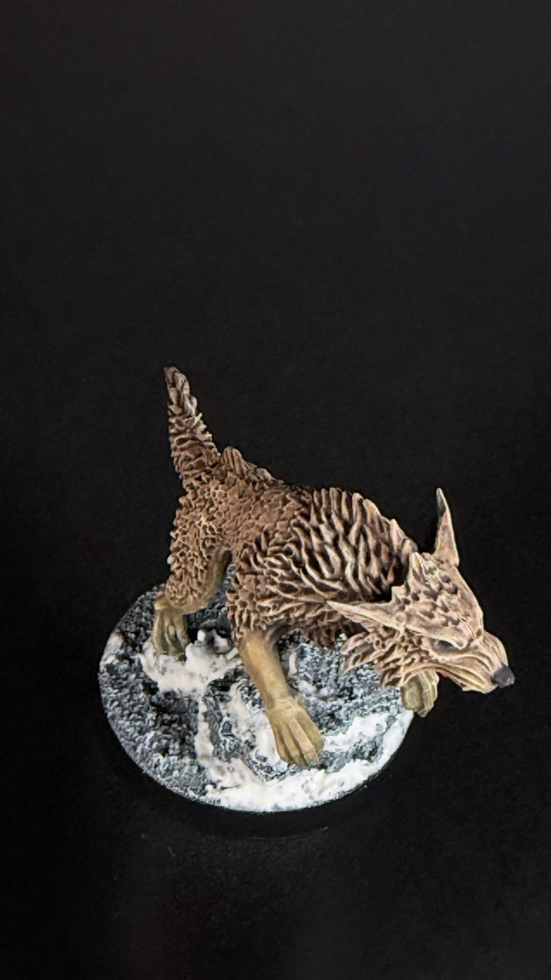 Brown dragon figurine perched on a snowy rocky base against a black background, detailed scales visible.