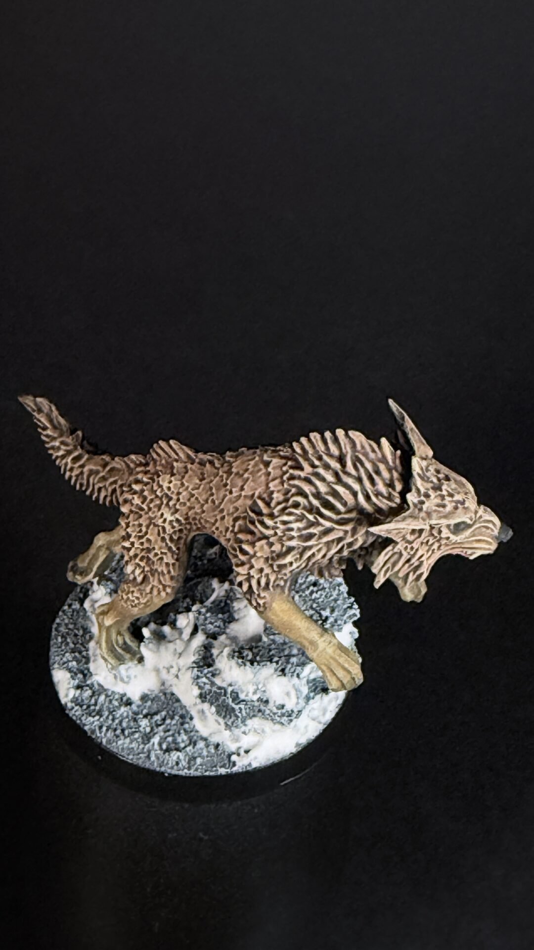 Brown dragon miniature with textured scales standing on a rocky pedestal against a black background