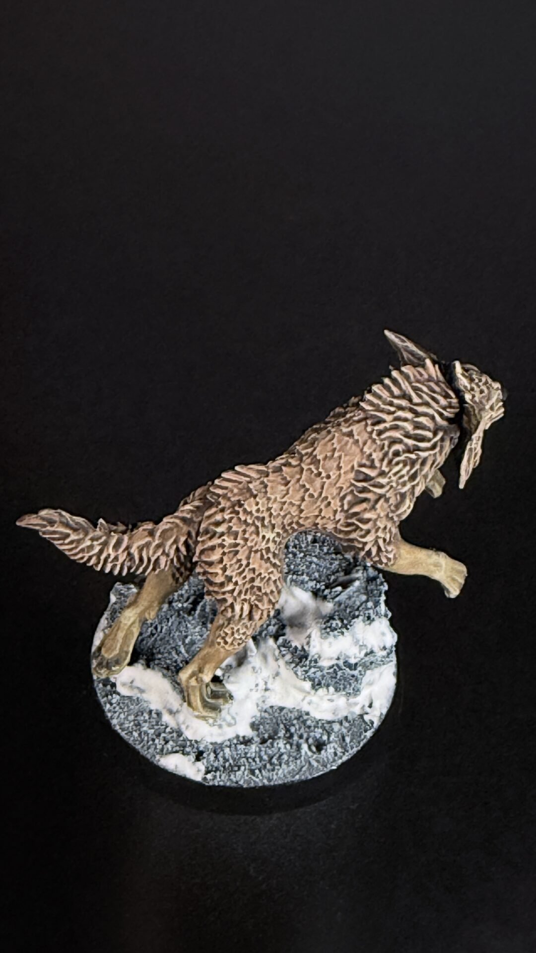 A detailed sculpture of a brown, striped four-legged animal perched on a rocky, snow-covered base against a black background.