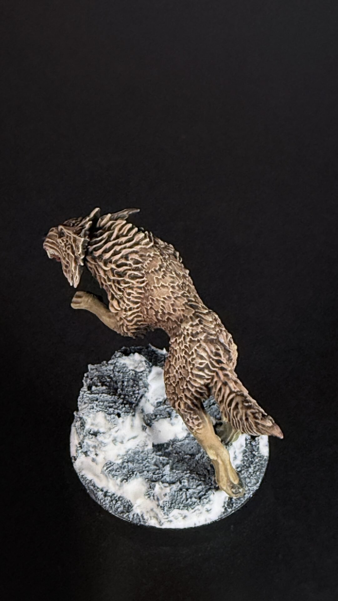 Brown, textured dragon-like figurine crawling over a snowy, rocky base on a black background.