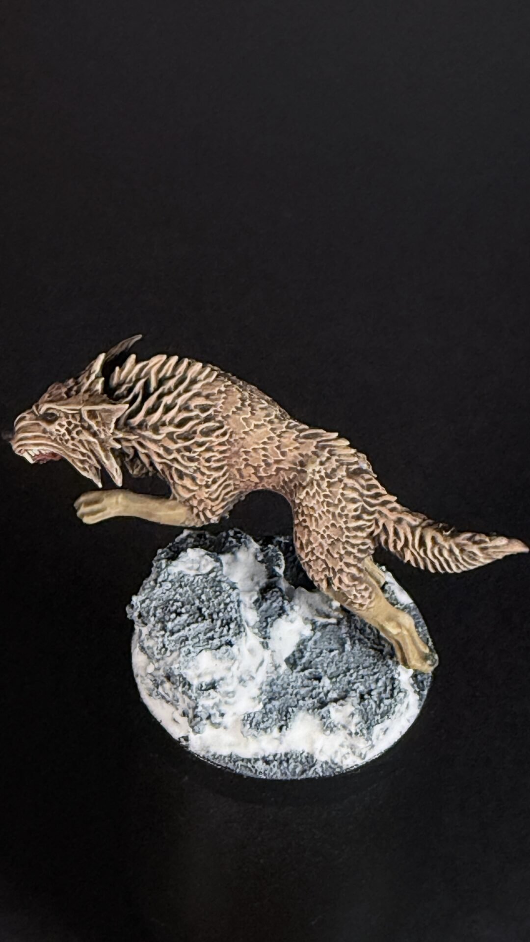 Brown textured dragon figurine perched on a snow-dusted rock against a black background.