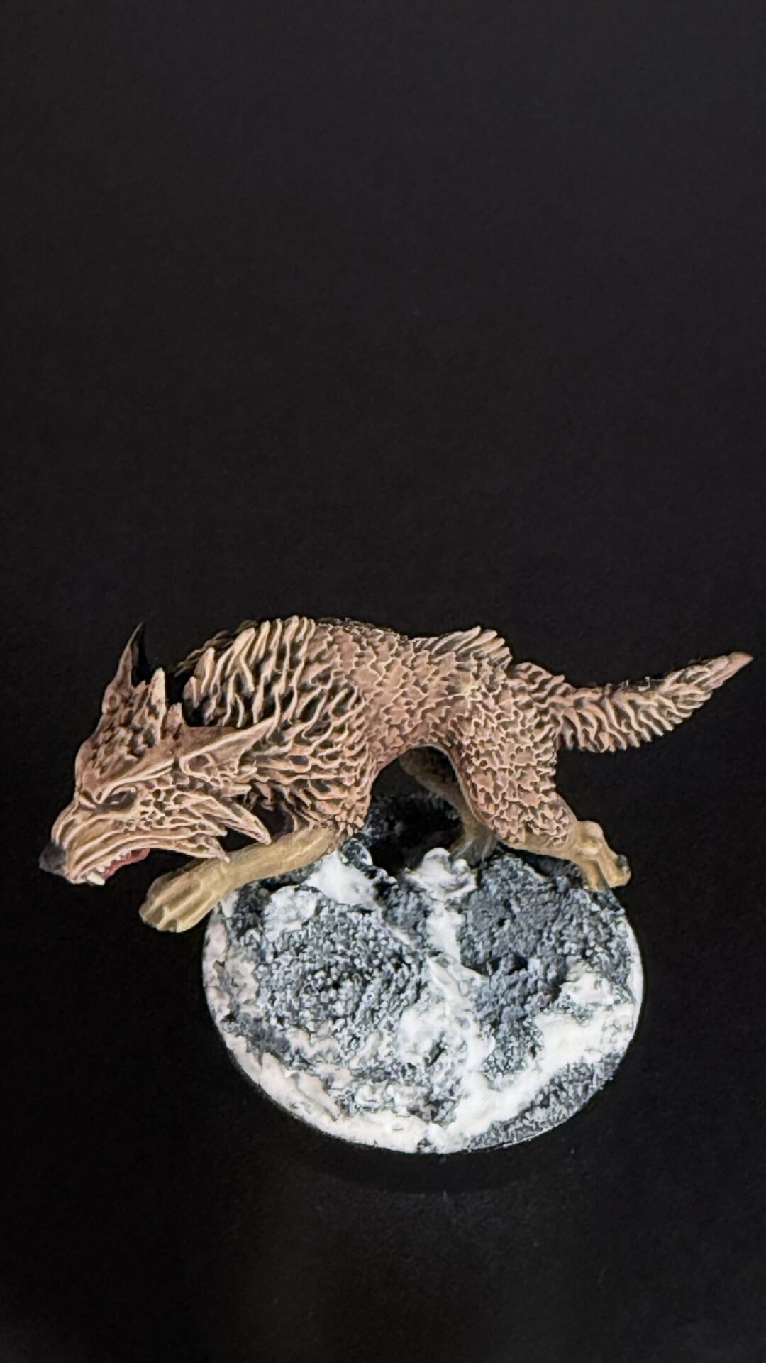 Brown dragon figurine with textured scales perched on a rocky base against a black background on display.