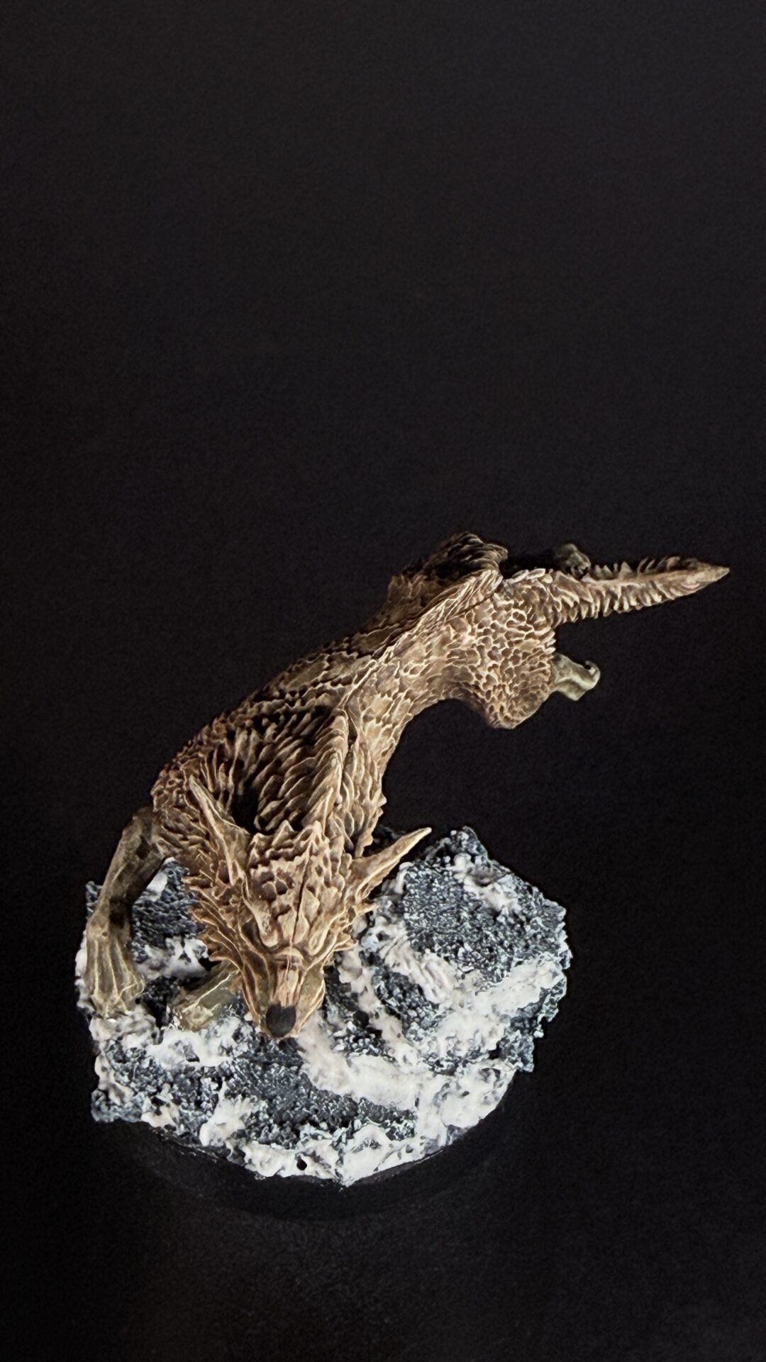 Detail of a brown dragon wing sculpture attached to a rocky base against a black background.