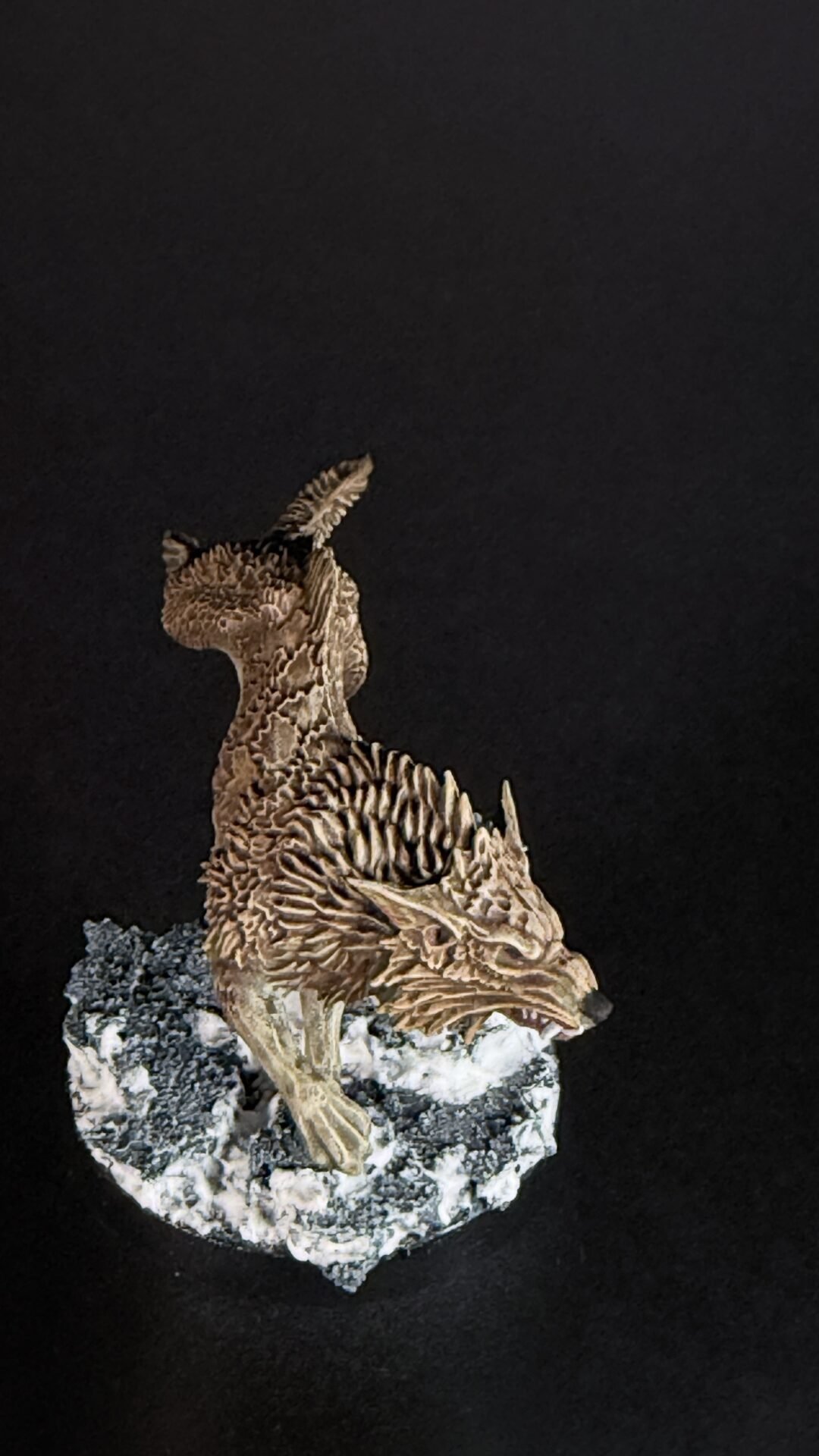Brown dragon statue with textured scales perched on a rocky base against a black background.