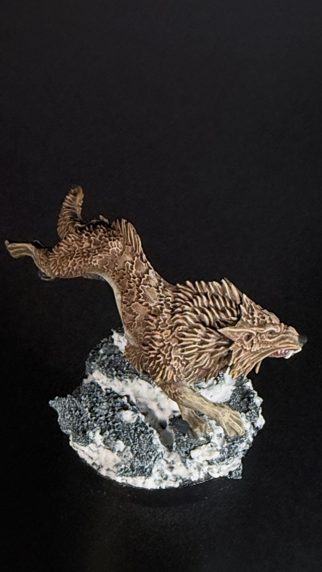 Brown textured dragon statue perched on a jagged rock against a black background, with its mouth open.