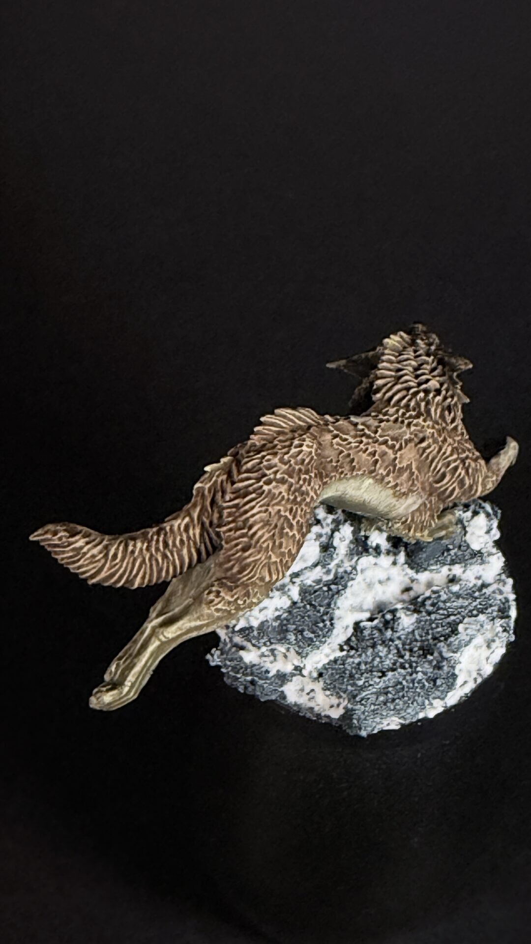 Feathered pterosaur sculpture perched on a jagged rock against a dark background, showing brown patterned wings and body.