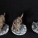 Three brown dragon sculptures perched on rugged grey rocks against a black background, viewed from the side.