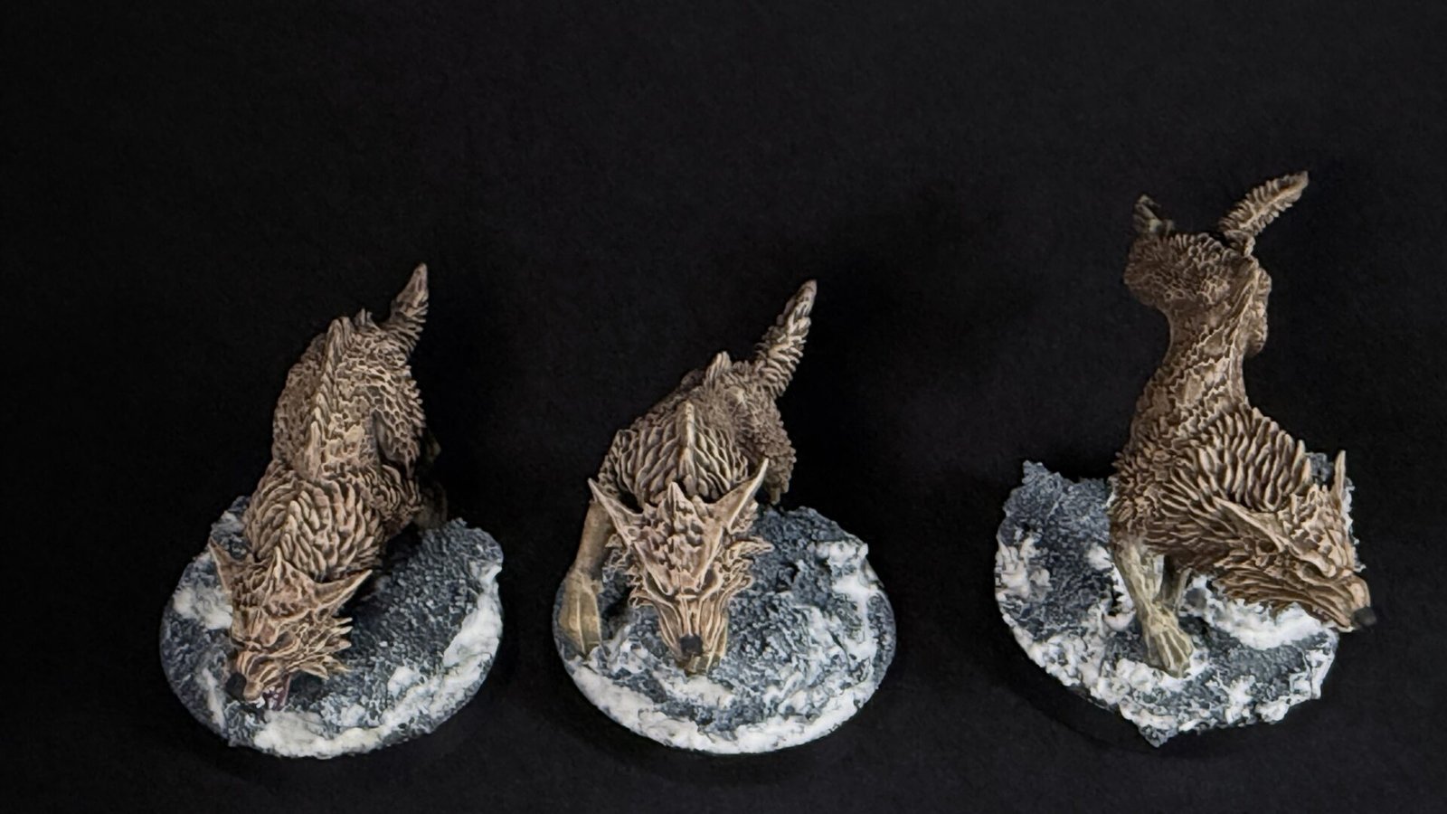Three brown dragon sculptures perched on rugged grey rocks against a black background, viewed from the side.