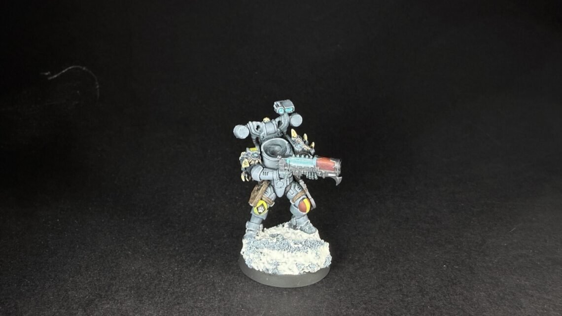 Painted sci‑fi armored miniature, holding a bulky rifle, standing on a rocky base against a black backdrop.
