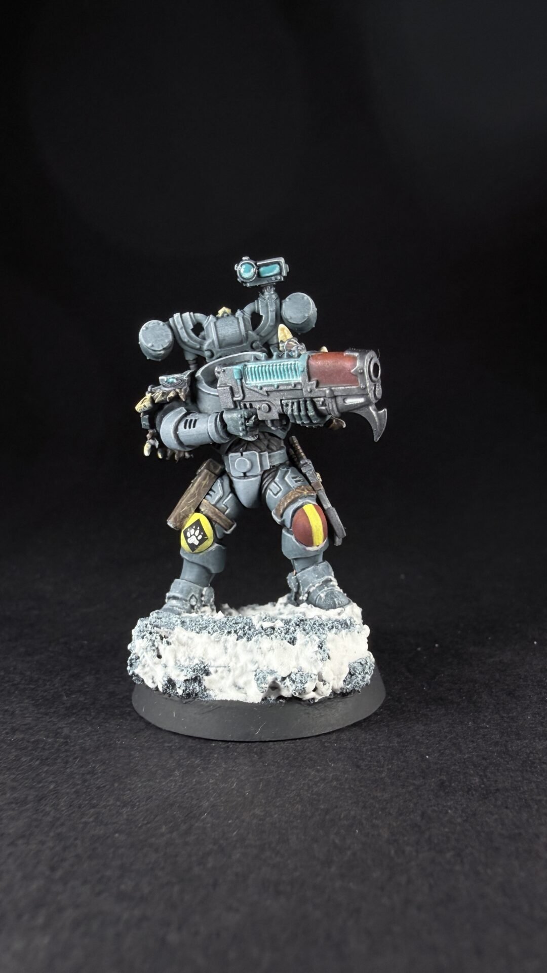 Armored sci-fi soldier miniature holding a large gun, standing on a snowy rocky base against a black background