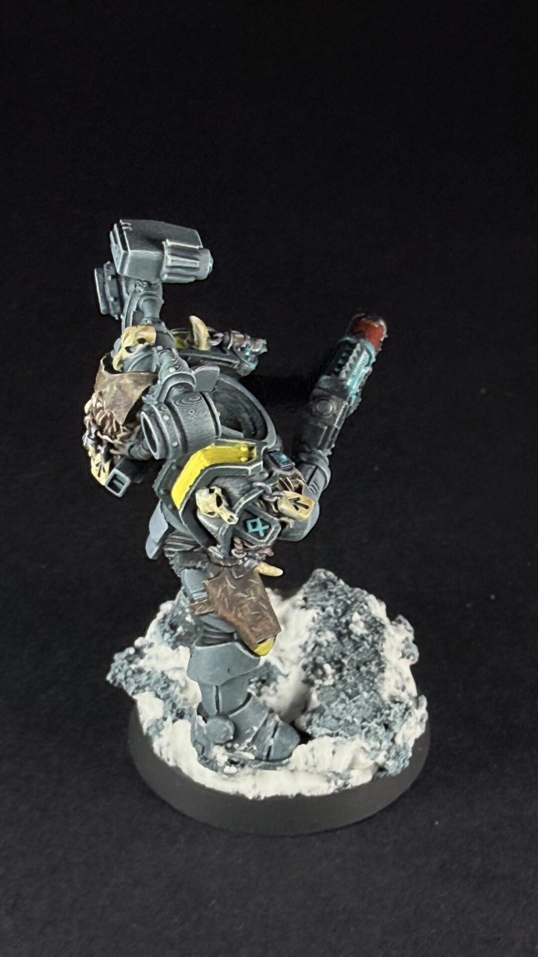 A detailed sci‑fi armored miniature on a snowy rocky base, wielding a large gun with a yellow visor and mechanical backpack pieces.