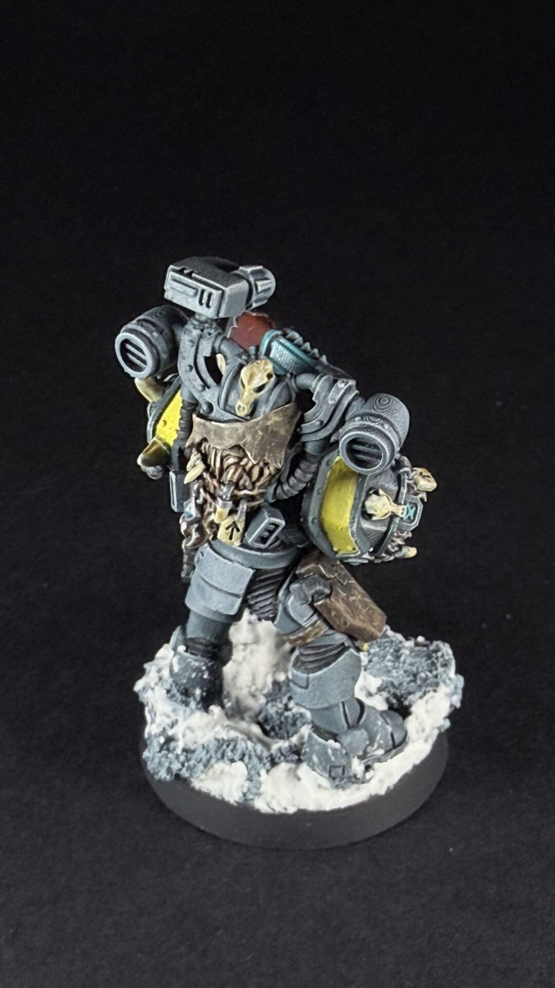 Miniature sci‑fi space marine in gray armor with skulls and yellow highlights, standing on a snowy base against a dark background.