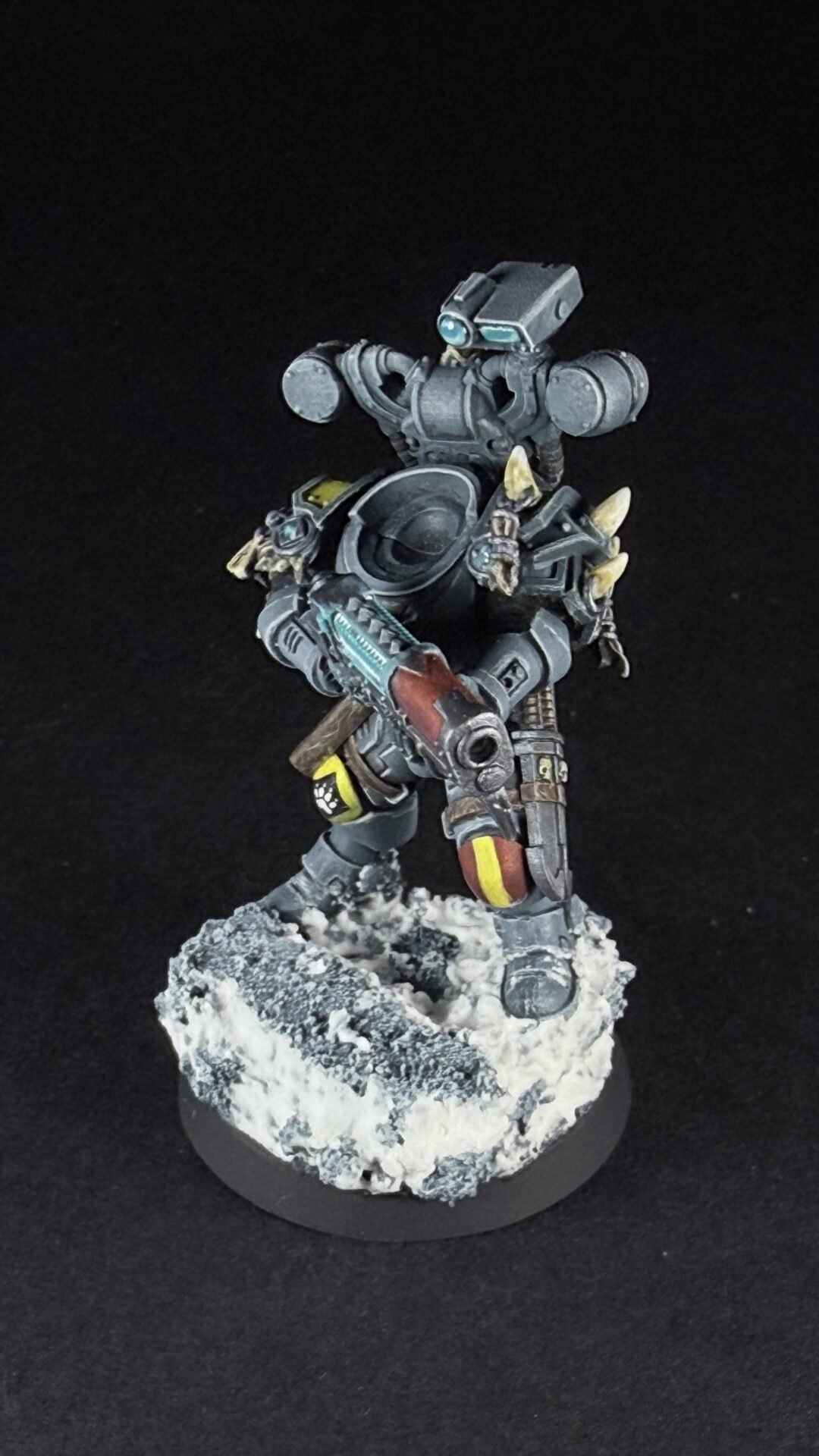 Armored sci-fi bipedal robot figure holding a rifle, standing on a snowy rocky base against a black background.