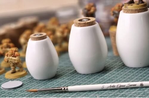 Miniature painting workspace with small toy soldiers, cork stoppers, and a brush on a green cutting mat.