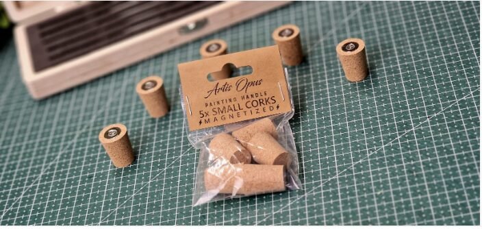 Bag of five small corks for magnetic handles on a green cutting mat, with loose corks scattered nearby and a label visible on the bag.