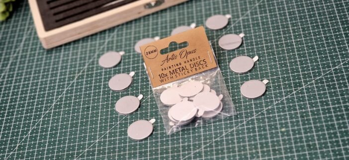 Bag of small white circular metal discs with sticky backs on a green cutting mat, used for crafts.